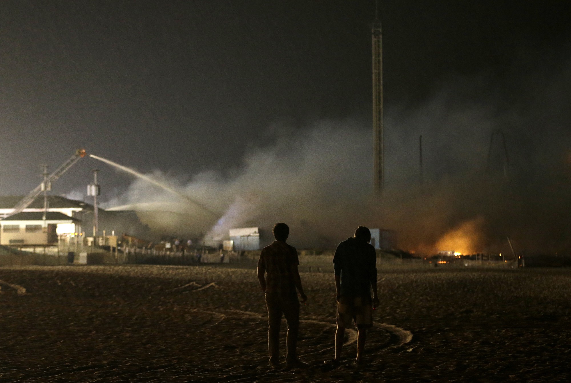Nicholas Wey, 18, left, and his best friend Peter Irler, 18, both from Toms River, N.J., stand on the beach while looking at a fire that burns a large portion of the Seaside Park boardwalk Thursday in Seaside Park, N.J. The fire, which apparently started in the area of an ice cream shop and spread several blocks, hit the recently repaired boardwalk, which was damaged last year by Superstorm Sandy.