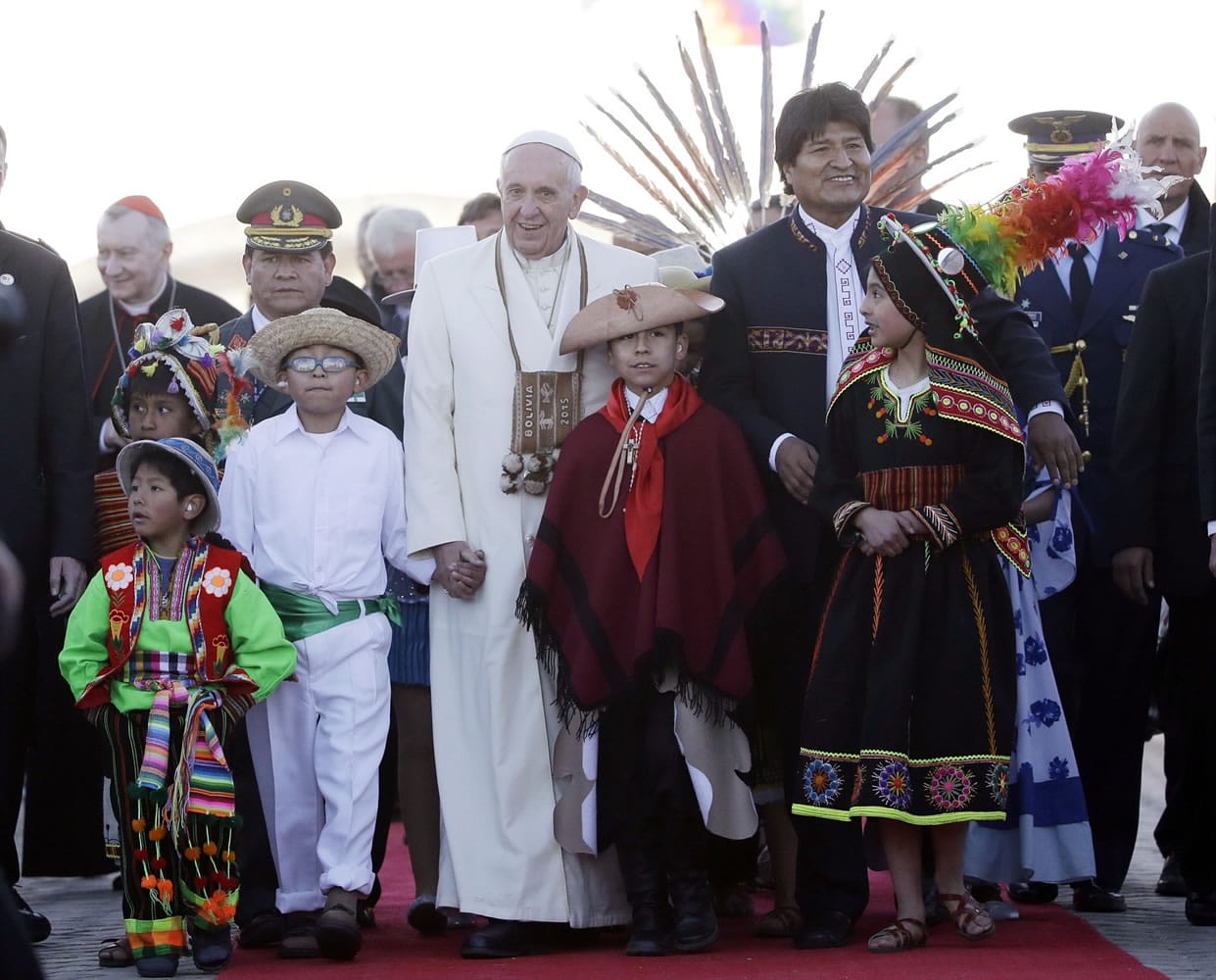 Pope Francis holds hands with children wearing traditional costumes as he walks with Bolivian President Evo Morales upon his arrival at the El Alto airport, Bolivia, Wednesday, July 8, 2015. The pouch Francis is wearing around his neck was given to him by Morales. It's woven of alpaca with indigenous trimmings and traditionally used by people in the Andes to hold coca leaves, which they chew to ward off the ill effects of extreme altitude. Due to the altitude, the pope will spend only a few hours in the capital city La Paz, during his South American tour. Bolivia is the second of three countries Francis will be visiting on his South American tour.