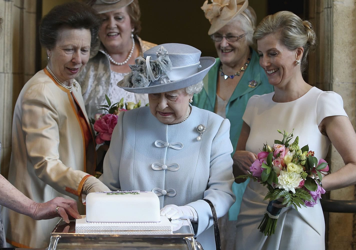 Britain's Sophie, Countess of Wessex, right, and Princess Anne, left, look on as Queen Elizabeth II, center, prepares to cut a Women's Institute Celebrating 100 Years cake Thursday at the Centenary Annual Meeting of The National Federation of Women's Institute at the Royal Albert Hall in London.