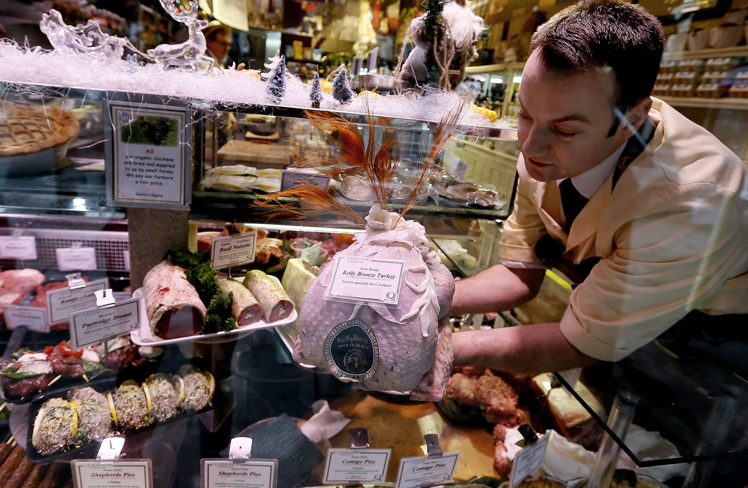 Seen through the window, Danny Lidgate places a turkey on display at his butcher shop Tuesday in Holland Park in London.