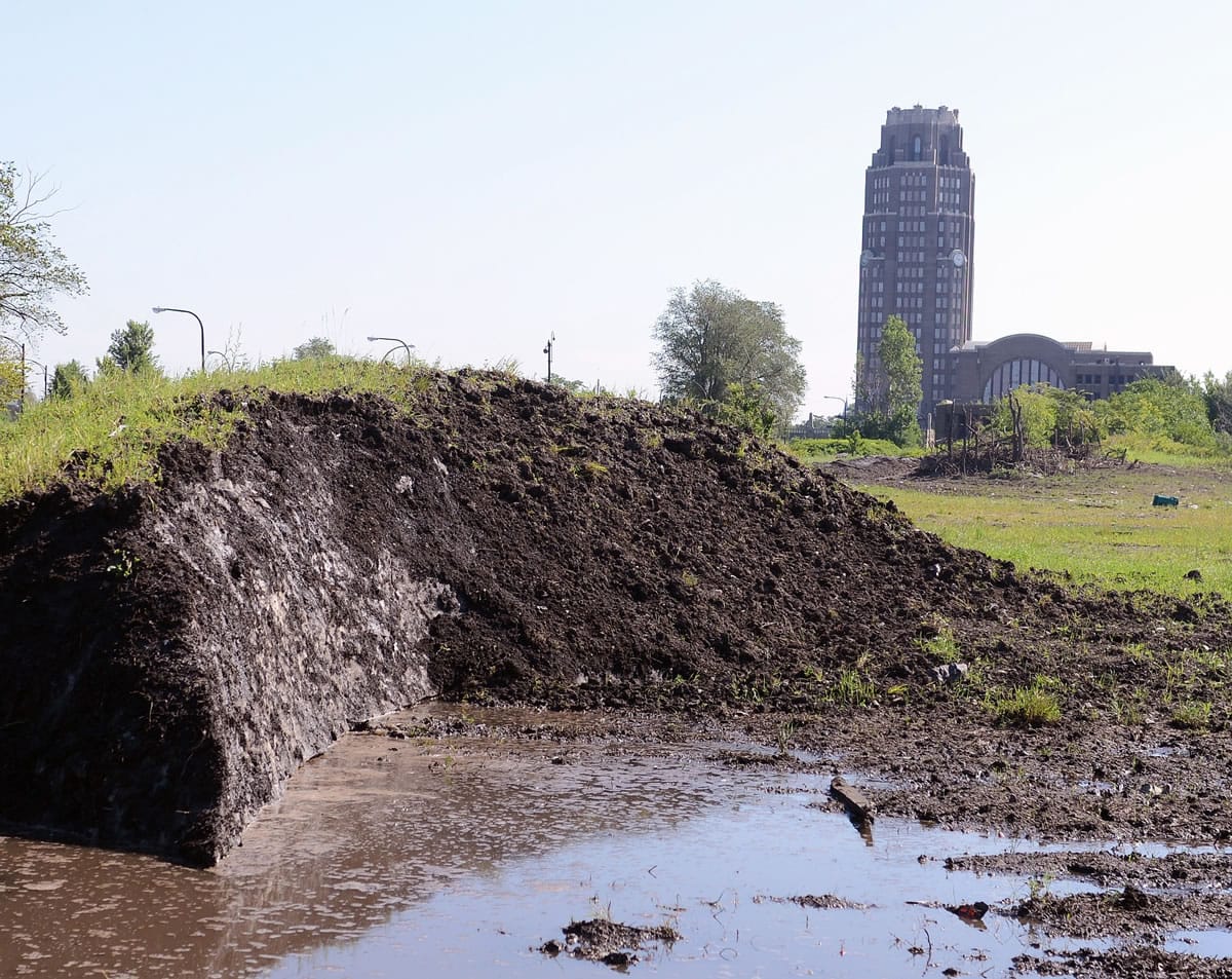A dirt covered snow pack, dumped eight months ago, creates pools of water as it slowly melts around the abandoned train station vacant lot in Buffalo, N.Y., Tuesday, July 28, 2015.  City crews dumped snow in the lots after a lake-effect storm dumped more than 7 feet on parts of Buffalo and the surrounding area last November.