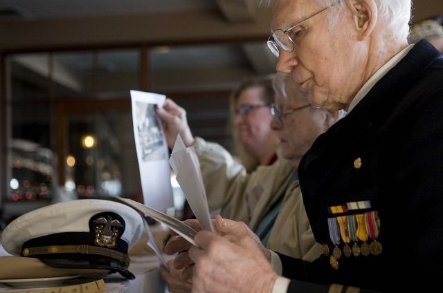 Pearl Harbor survivor Larry Lydon, from right, wife Bette Lydon and their granddaughter Anne Lydon-Beaton look through pictures of the attack on Pearl Harbor during Monday's memorial event at the Red Lion Inn at the Quay.