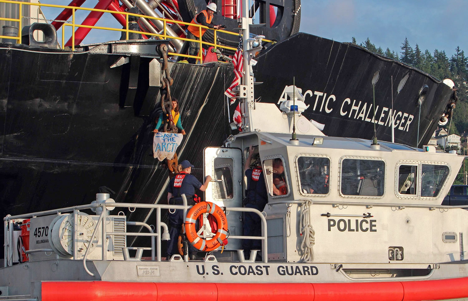 The Coast Guard stands by as a woman identified as Chiara D?Angelo has suspended herself Friday in a climbing harness from the anchor chain of the Royal Dutch Shell support ship Arctic Challenger in the harbor at Bellingham.