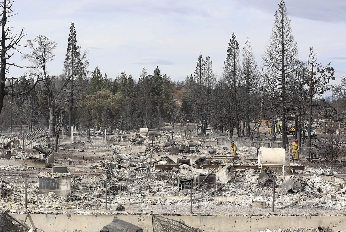 Firefighters, at right, walk amid a row of houses destroyed by a wildfire Tuesday in Weed, Calif.