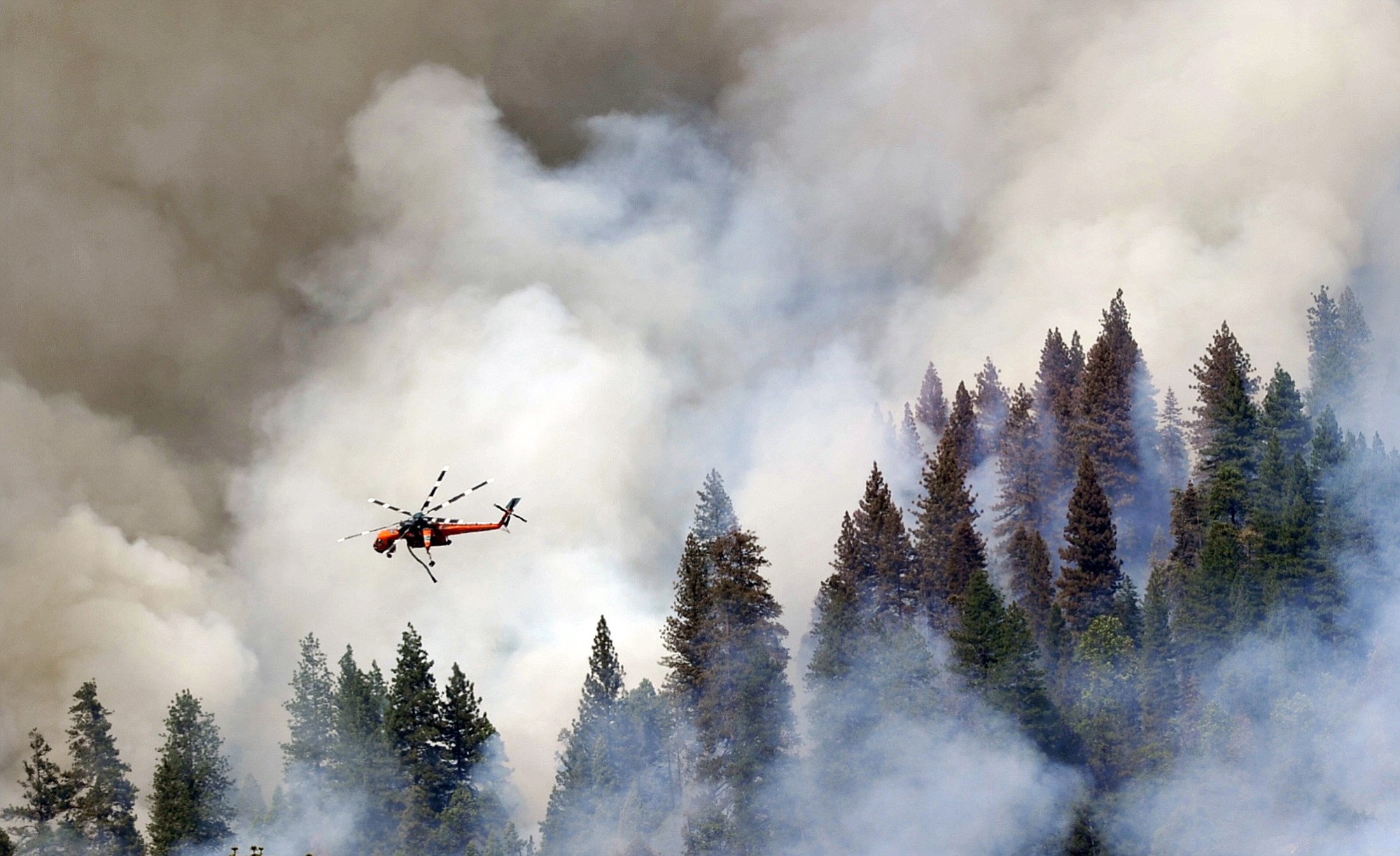 A helicopter flies over Willow Creek Canyon as a wildfire continues burning in the Sierra near Bass Lake, Calif., on Monday.