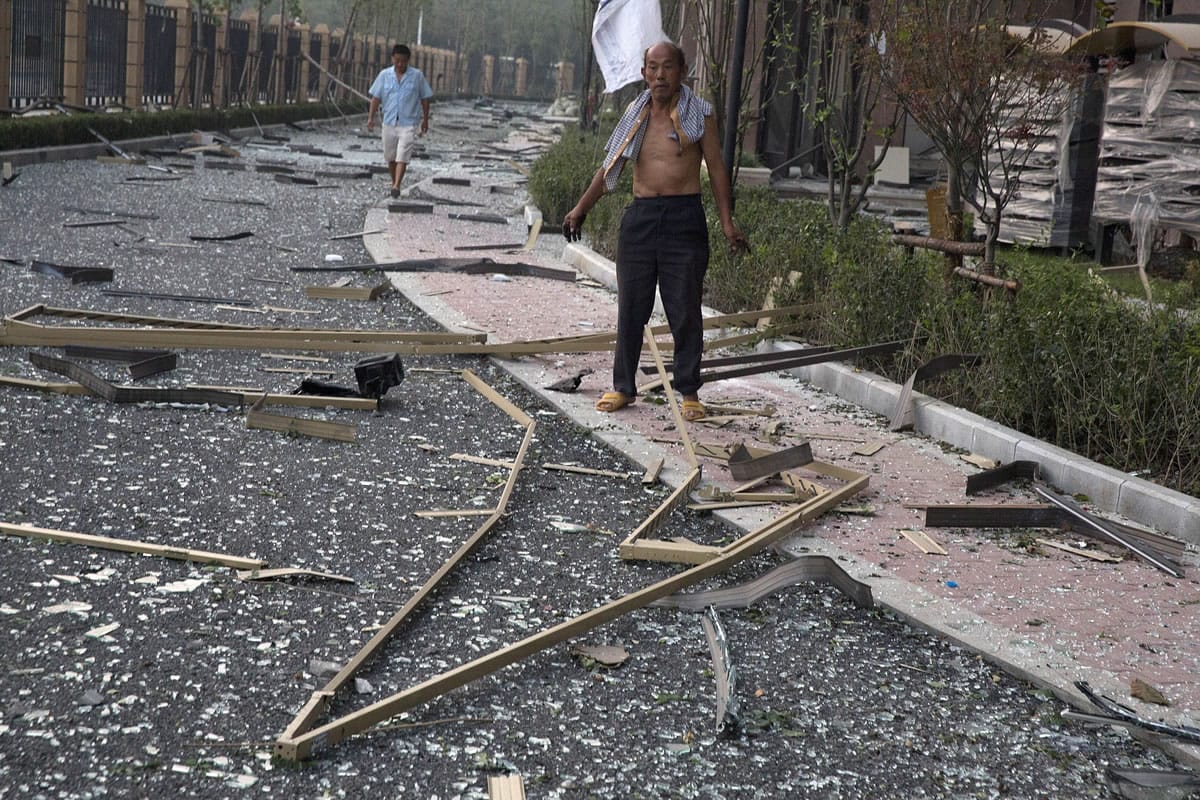 A man stands near broken glasses after a nearby explosion shattered windows at a residential compound, in China's Tianjin municipality, Thursday, Aug. 13, 2015. Huge explosions sparked overnight at a warehouse for dangerous materials in the northeastern Chinese port of Tianjin killed at least 13 people, injured hundreds and sent massive fireballs into the night sky, officials and state media outlets said Thursday.