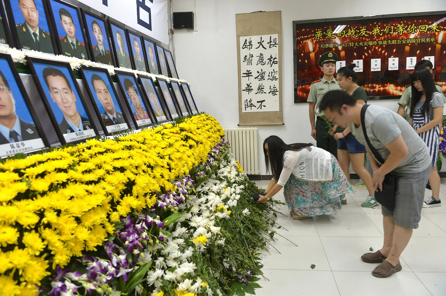 People mourn and place flowers at a memorial at a fire station in northeastern China's Tianjin municipality Tuesday, Aug. 18, 2015, for Chinese firefighters killed in a series of blasts at Tianjin's port. Thunderstorms on Tuesday complicated recovery efforts from last week's massive deadly explosions at a warehouse in Tianjin's port that exposed dangerous chemicals ? including some that could become flammable on contact with water.