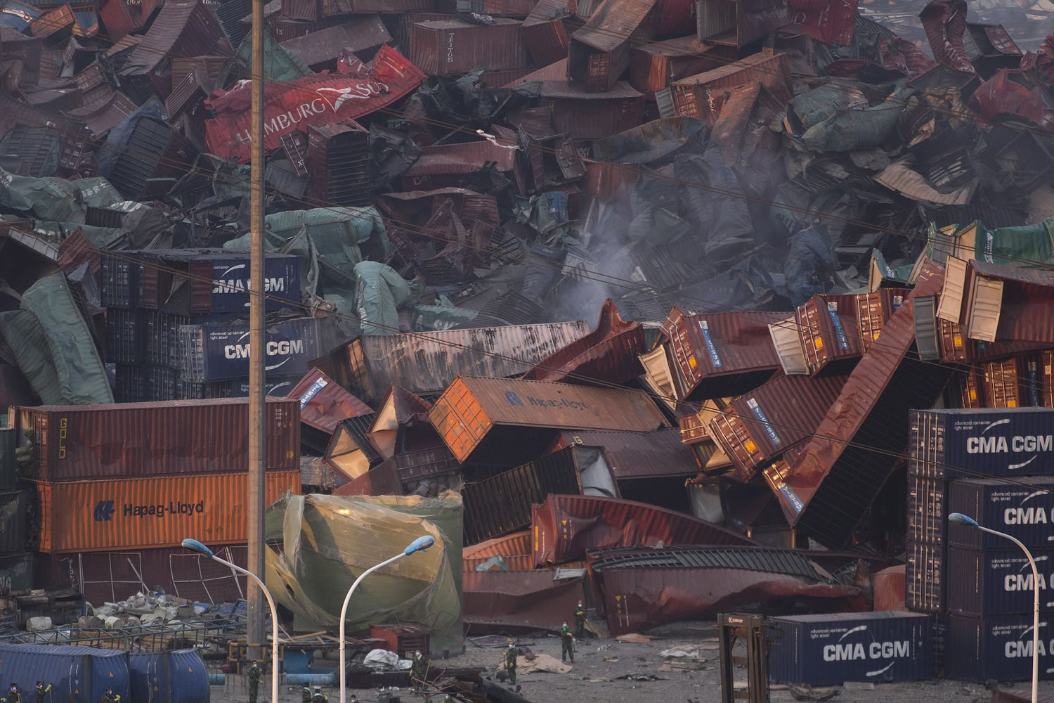 Workers sweep the area near deformed containers piled up after Wednesday's explosion in northeastern China's Tianjin municipality, Friday, Aug. 14, 2015. Rescuers pulled out a firefighter trapped for 32 hours after responding to a fire and huge explosions in the Chinese port city as authorities dealt Friday with a fire still smoldering amid potentially dangerous chemicals.