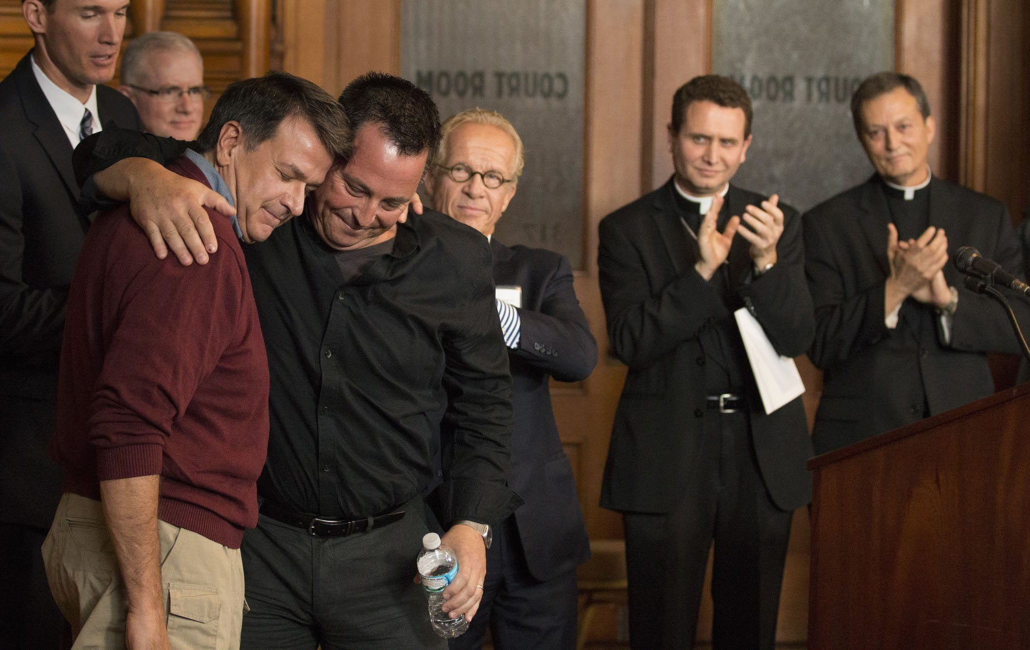 Abuse survivors Al Michaud, left, and Jim Keenan embrace after they both spoke of the importance of this historic agreement as attorney Jeff Anderson, Bishop Andrew Cozzens and Vicar General Rev. Charles Lachowitzer at right look on in St. Paul, Minn., Monday, Oct. 13, 2014. A Minnesota judge signed off on a settlement in a groundbreaking case that accused Catholic church leaders in Minnesota of creating a public nuisance by failing to warn parishioners about an abusive priest.