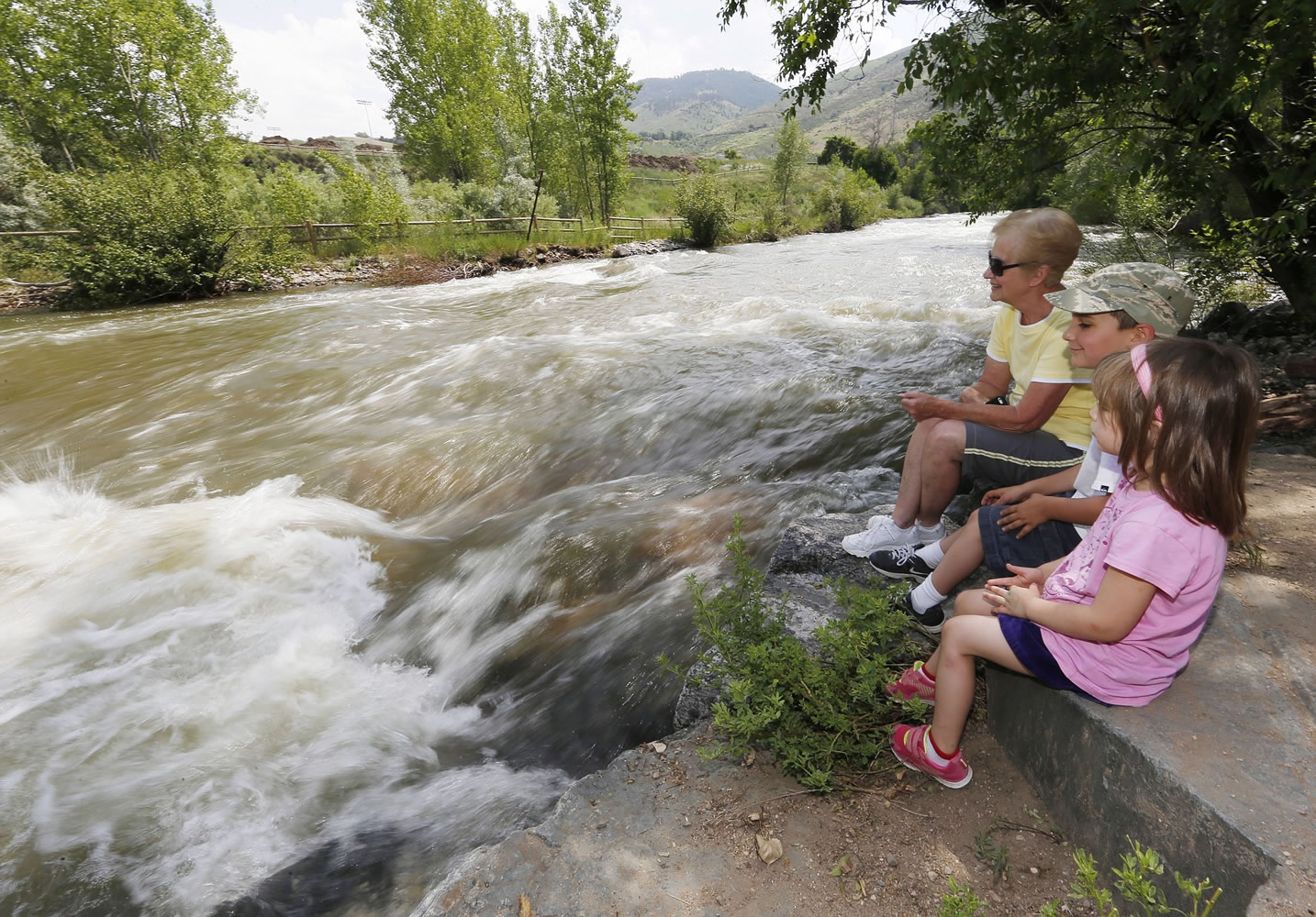 Carol Johnston, at rear, sits with her grandchildren, Olivia, front, and Anthony Villano as water in Clear Creek rushes by Tuesday in Golden, Colo.
