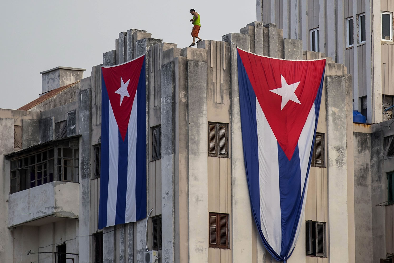 A man walks along the ledge of a building after hanging two giant Cuban flags, next to the U.S.