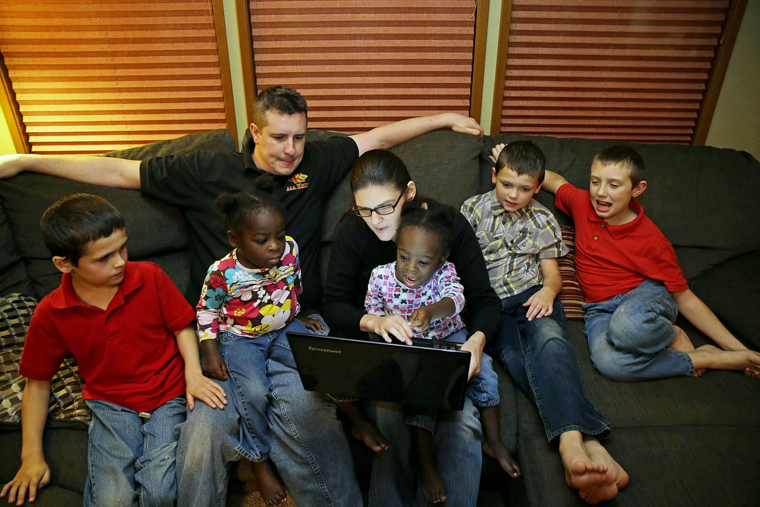 Joel and Tessa Sanborn hold their adopted twins, Favor, right, and Faith, left, 2, as they sit with their siblings and look at a computer photo of the twins' older brother Devine in Maple Valley.