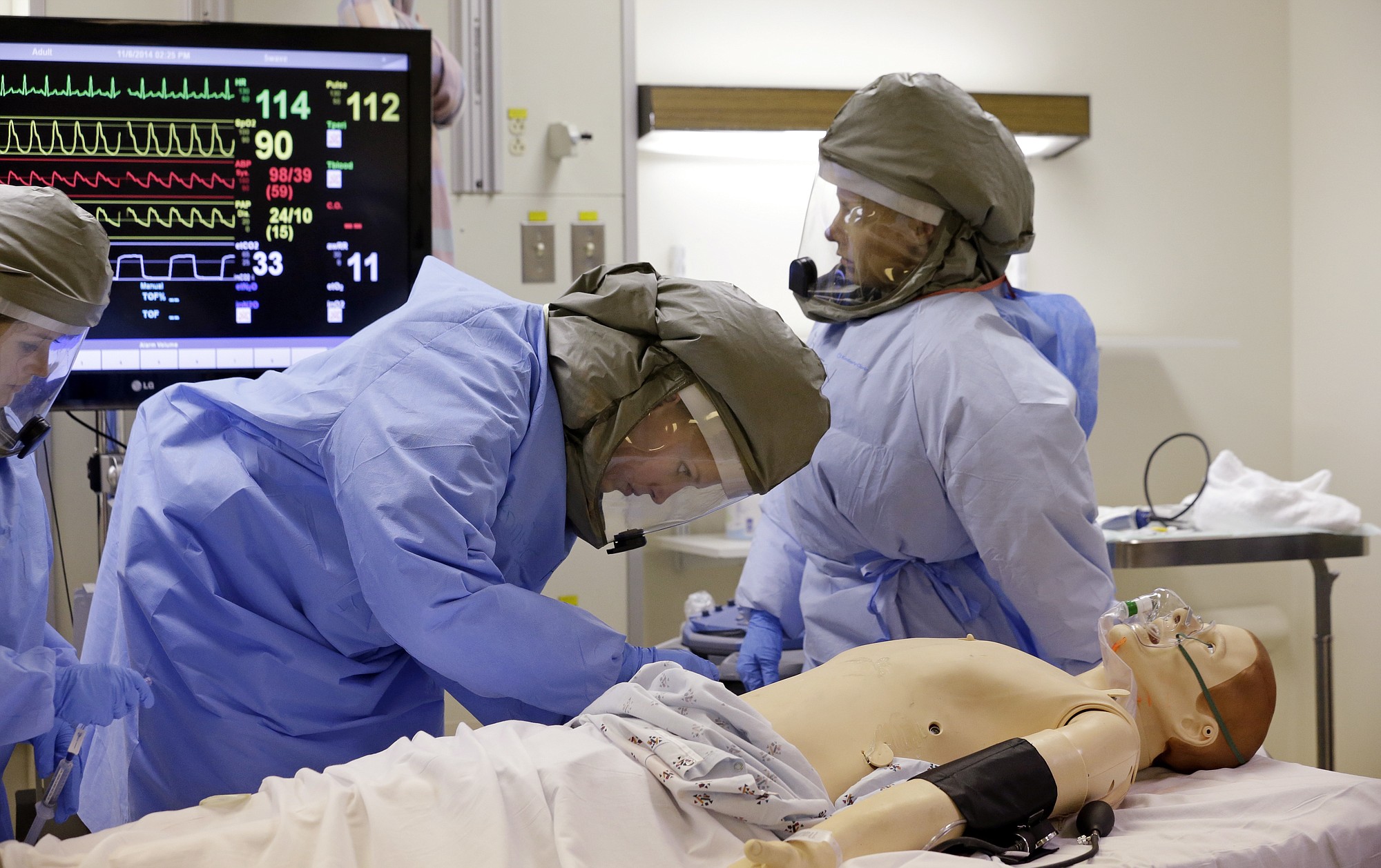 Medical workers wearing protective equipment surround and monitor a simulated patient Thursday during a demonstration for media members on their training for working with possible Ebola patients at Madigan Army Medical Center on Joint Base Lewis McChord, near Tacoma. Madigan providers and nurses have been training to perform clinical skills, including inserting IVs, obtaining blood samples for testing and conducting ultrasounds while dressed in powered air purifying respirators, impermeable suits and multiple layers of gloves. The clinically focused exercises use realistic patient simulators that speak through microphones and can express simulated bodily fluids.