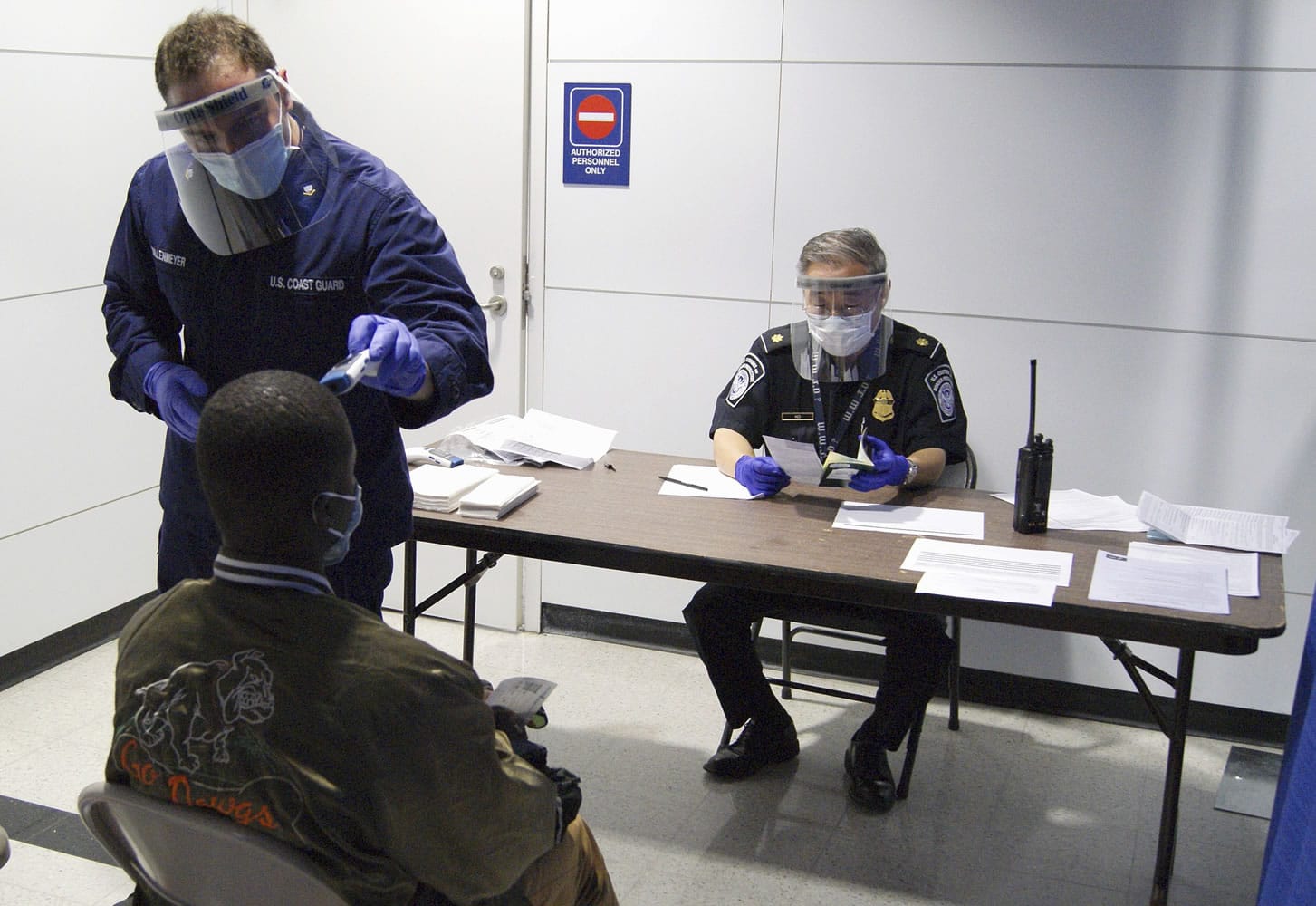 U.S. Coast Guard Health Technician Nathan Wallenmeyer, left, and CBP supervisor Sam Ko, right, conduct prescreening measures on a passenger who has arrived from Sierra Leone at O'Hare International Airport's Terminal 5 in Chicago. Demands are rising in Washington for the U.S.