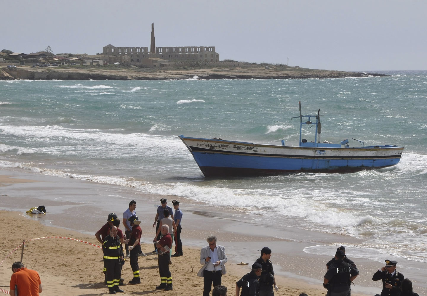 Police officers and firefighters stand by the boat, in background, that carried a group of migrants, after many drowned as they tried to reach the shore in Scicli, Sicily, Italy, in 2013.