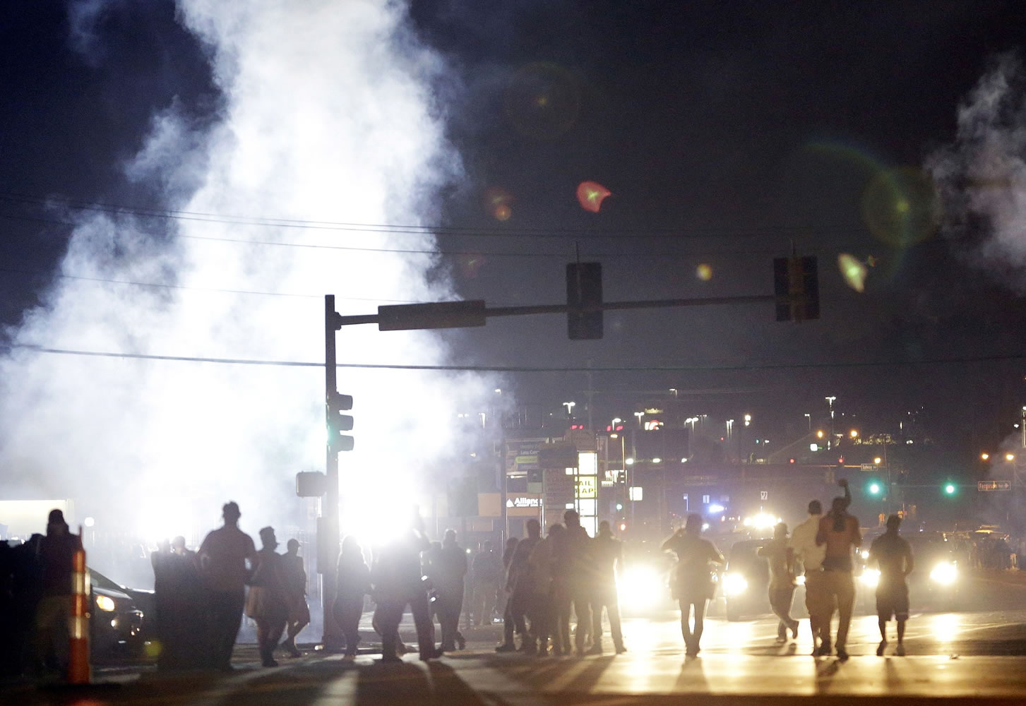 FILE - In this Monday, Aug. 18, 2014 file photo, people stand near a cloud of tear gas in Ferguson, Mo. during protests for the Aug. 9 shooting of unarmed black 18-year-old Michael Brown by a white police officer. The U.S. government agreed to a police request to shut down several miles of airspace surrounding Ferguson, even though authorities said their purpose was to keep media helicopters away during protests in August, according to recordings of air traffic control conversations obtained by The Associated Press.