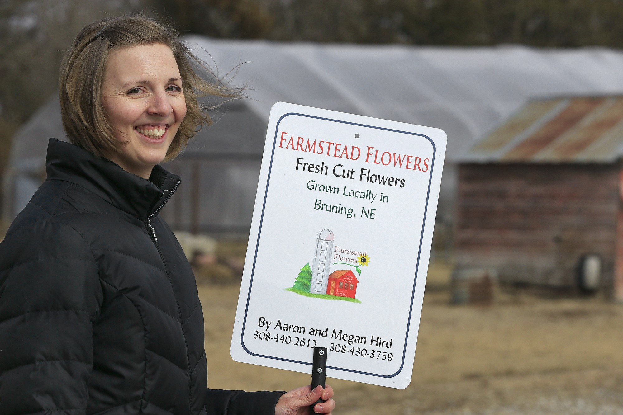 Megan Hird, owner of Farmstead Flowers, poses with a sign in front of her greenhouse in Bruning, Neb.