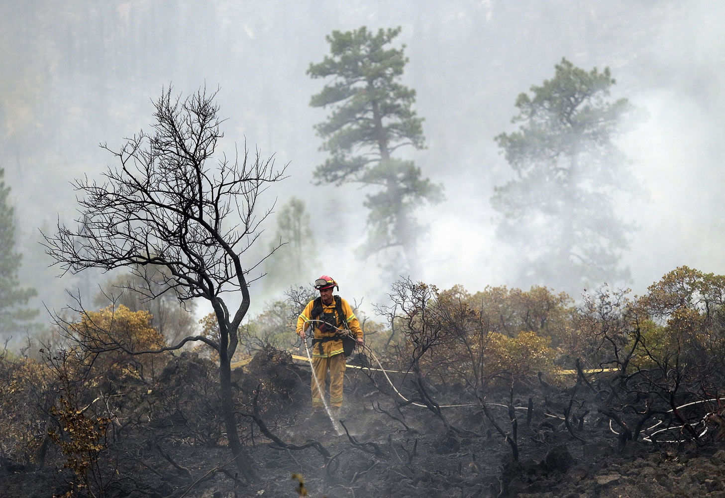 A firefighter with the Anderson, Calif., Fire Protection District dousing hot spots left behind by the Eiler Fire near Burney, Calif.