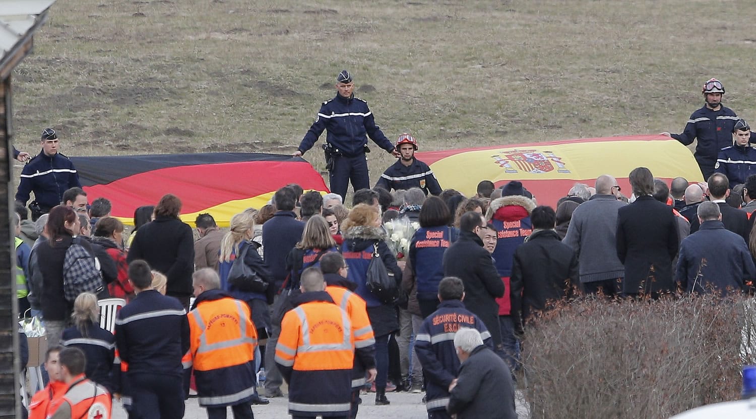 French gendarmes hold German and Spanish flags as family members of people involved in the Germanwings jetliner that crashed Tuesday in the French Alps attend a gathering in Le Vernet, Thursday, March 26, 2015. French prosecutors' assertion that this week's air crash of a German airliner into a rugged mountainside was a deliberate act of the co-pilot points to the possible need for a third pilot in airline cockpits, several aviation safety experts said Thursday.