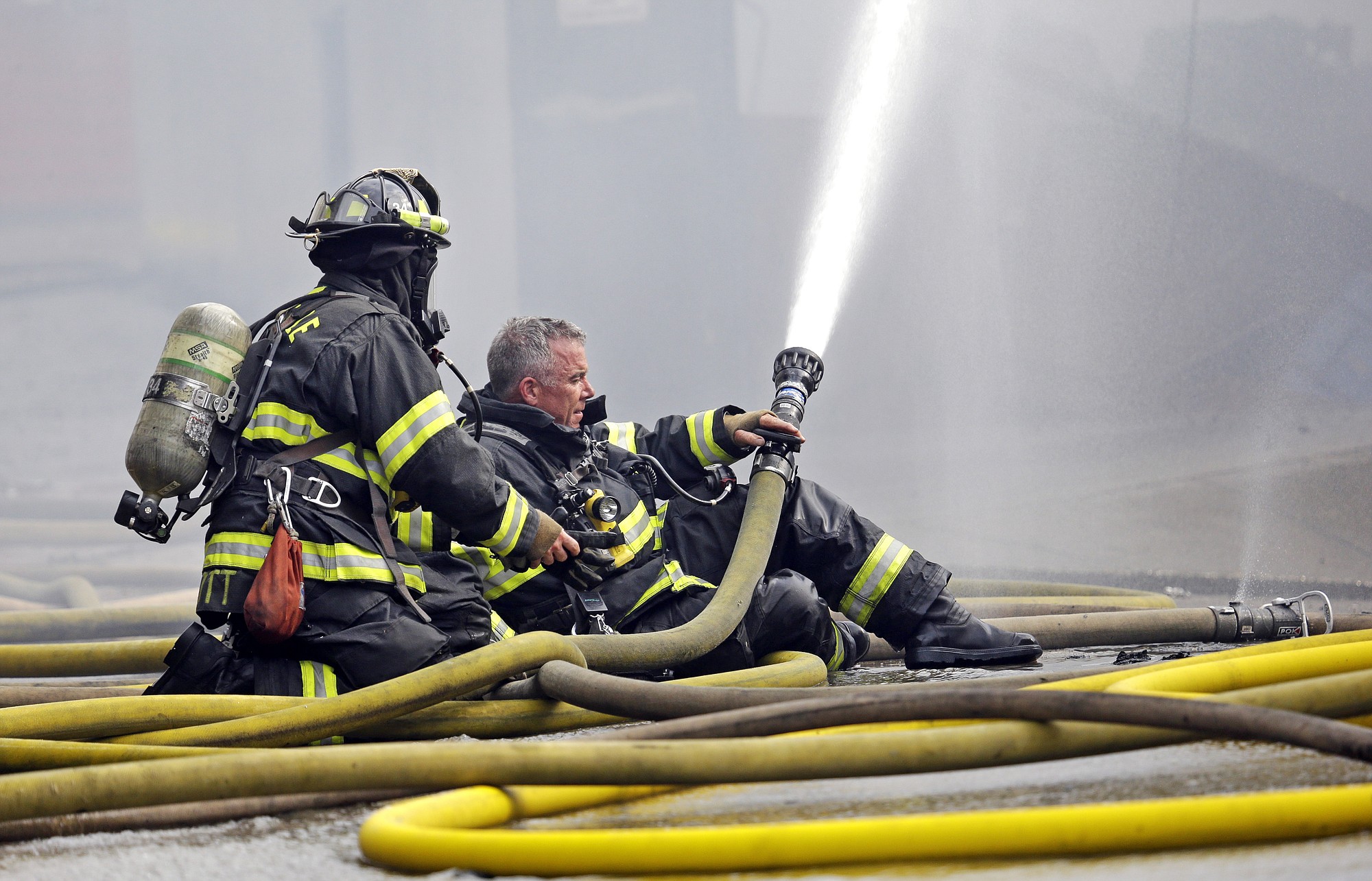 A firefighter briefly goes without his helmet as he prepares to put on a mask while hosing down a building on fire Tuesday in Seattle's Fremont neighborhood. No injuries were reported in the fire, which sent flames bursting through the roof of the building and created a large plume of smoke visible from downtown.