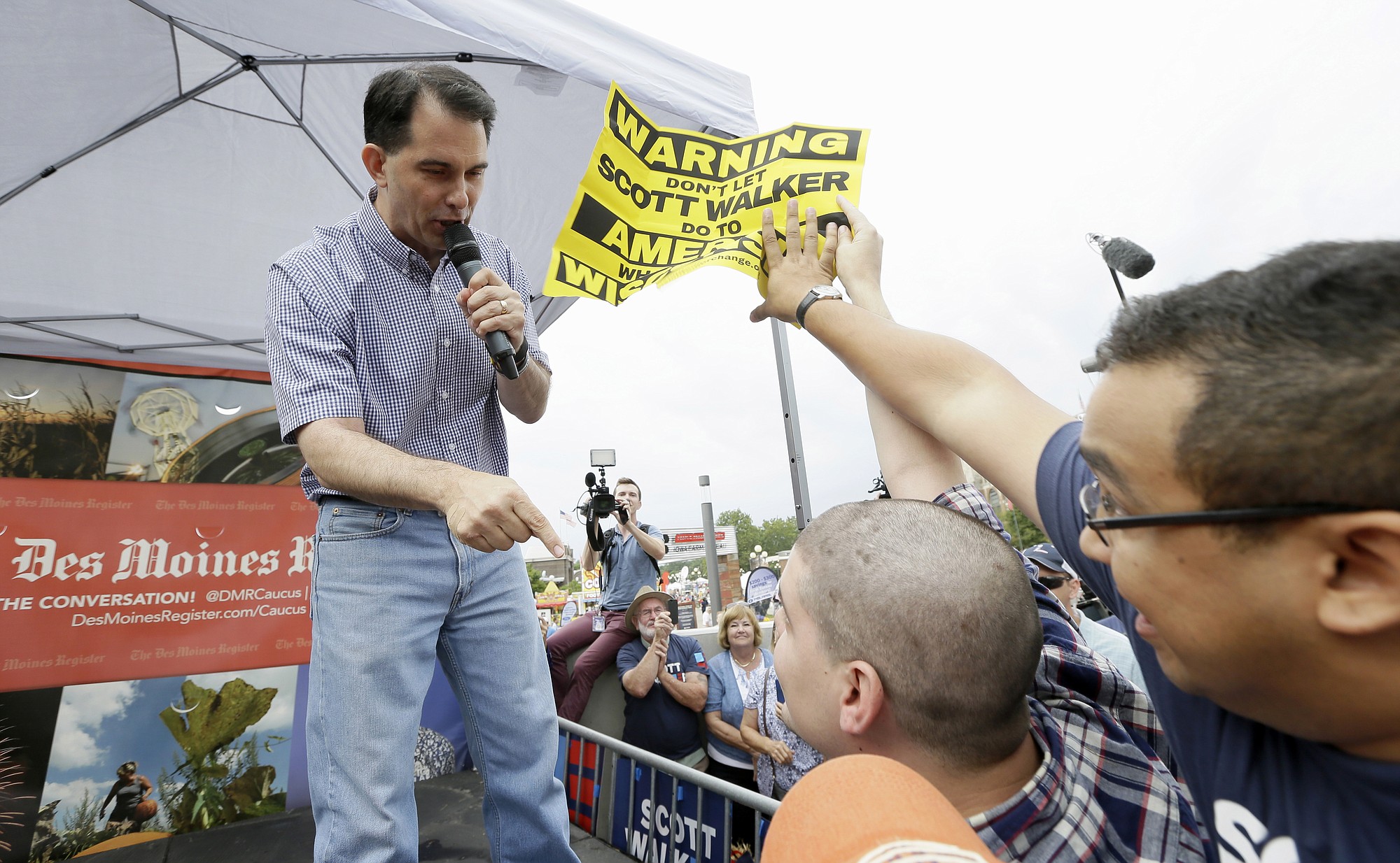 Republican presidential candidate, Wisconsin Gov. Scott Walker talks to a protestor as a supporter grabs his sign during a visit to the Iowa State Fair, Monday, Aug. 17, 2015, in Des Moines, Iowa.