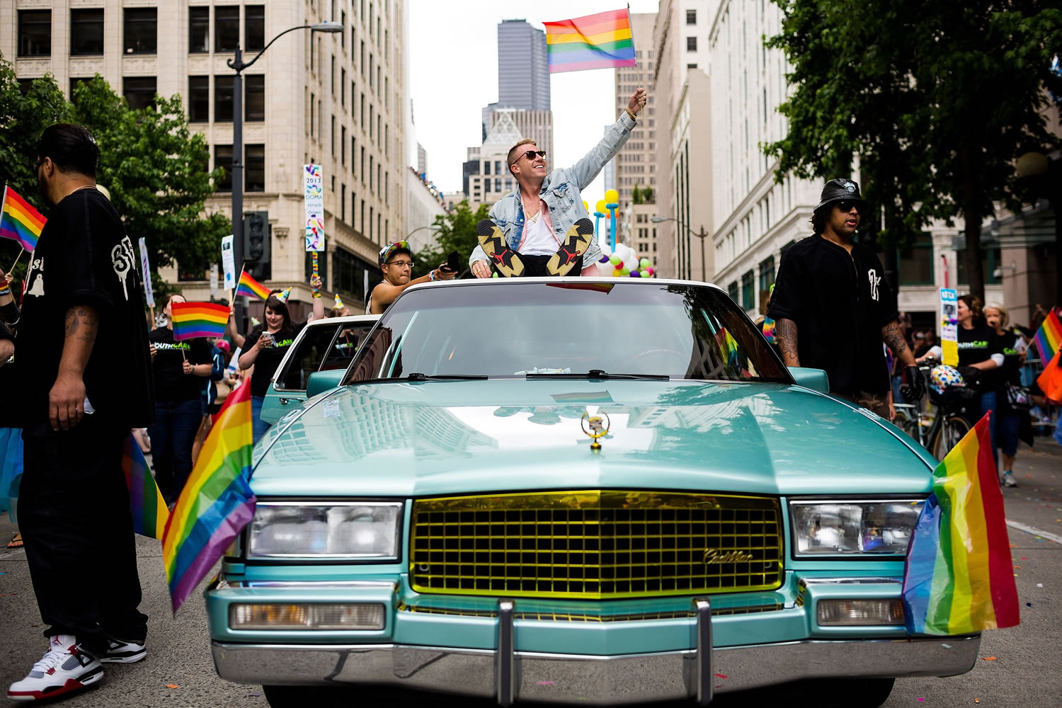 Waving a pride flag, Seattle rap artist Macklemore, center, rides atop his Cadillac through the 40th annual Seattle Pride Parade on Sunday in Seattle.