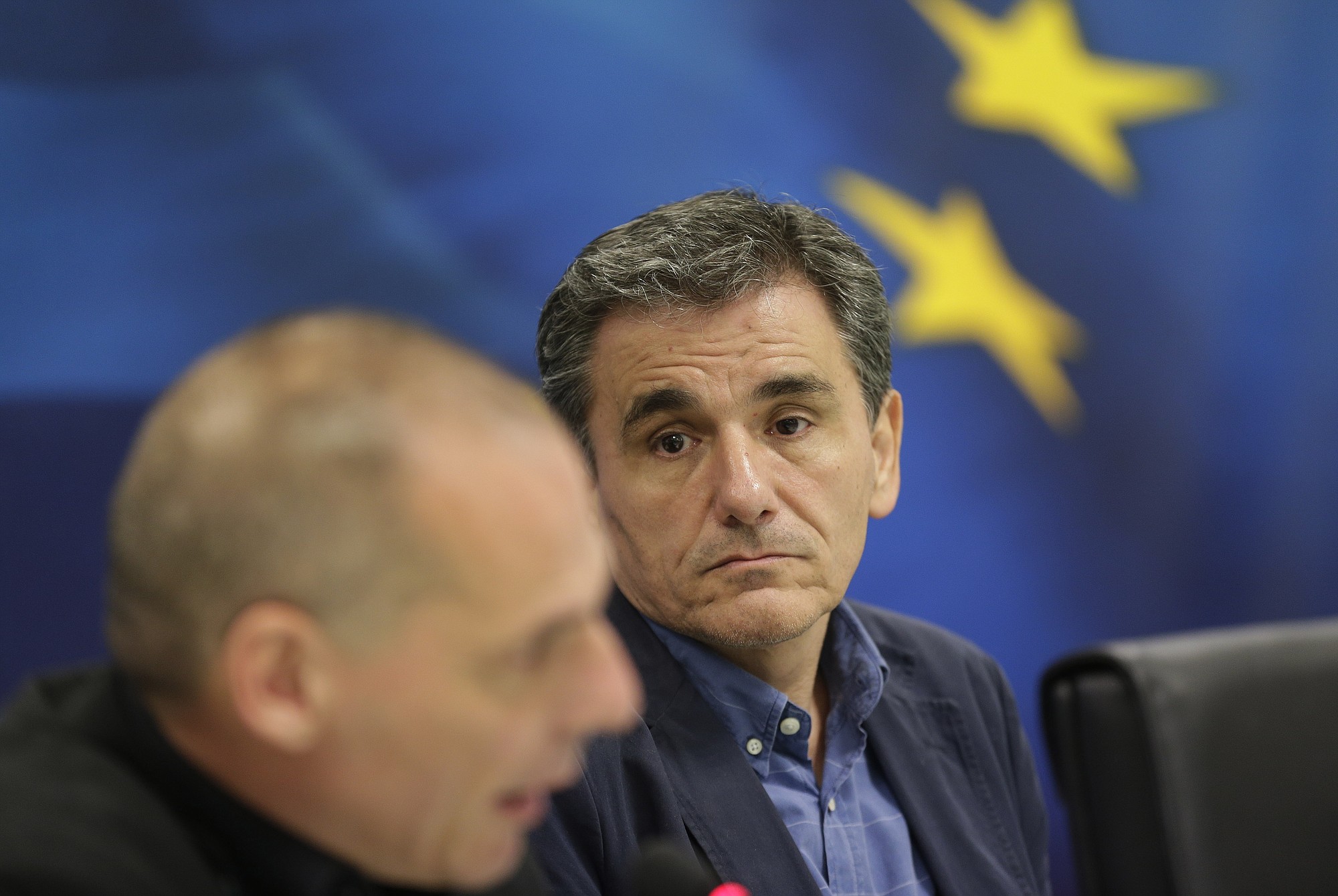 New Greek Finance Minister Euclid Tsakalotos, right, listens to outgoing Finance Minister Yanis Varoufakis as he speaks Monday during a ceremony in Athens.