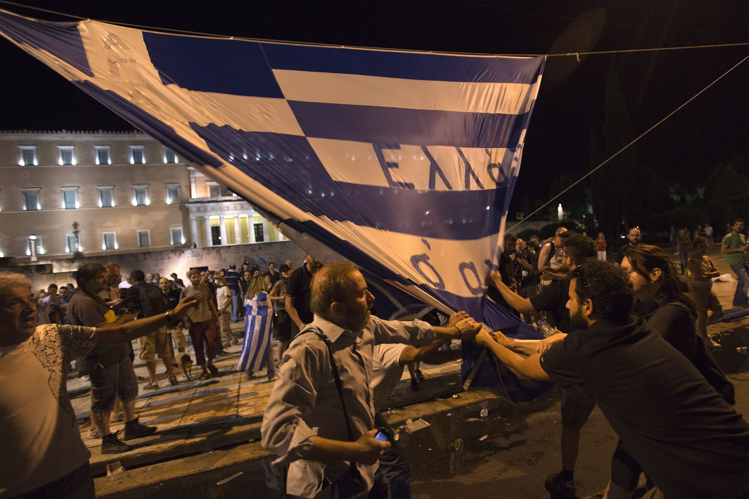 Protesters scuffle with each other to tear down a Greek flag with a writing reading ''Greece we love you'' during a rally outside the Greek Parliament in Athens, Wednesday, July 15, 2015. Greece's prime minister was fighting to keep his government intact in the face of outrage over an austerity bill that parliament must pass Wednesday night if the country is to start negotiations on a new bailout and avoid financial collapse.