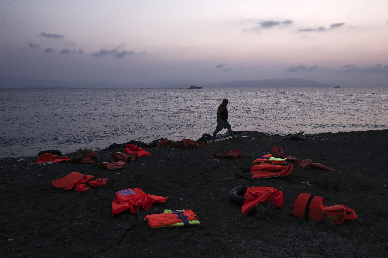 A man walks amid life vests which have been left by migrants after disembarking at a coast on the southeastern island of Kos, Greece, on Tuesday.
