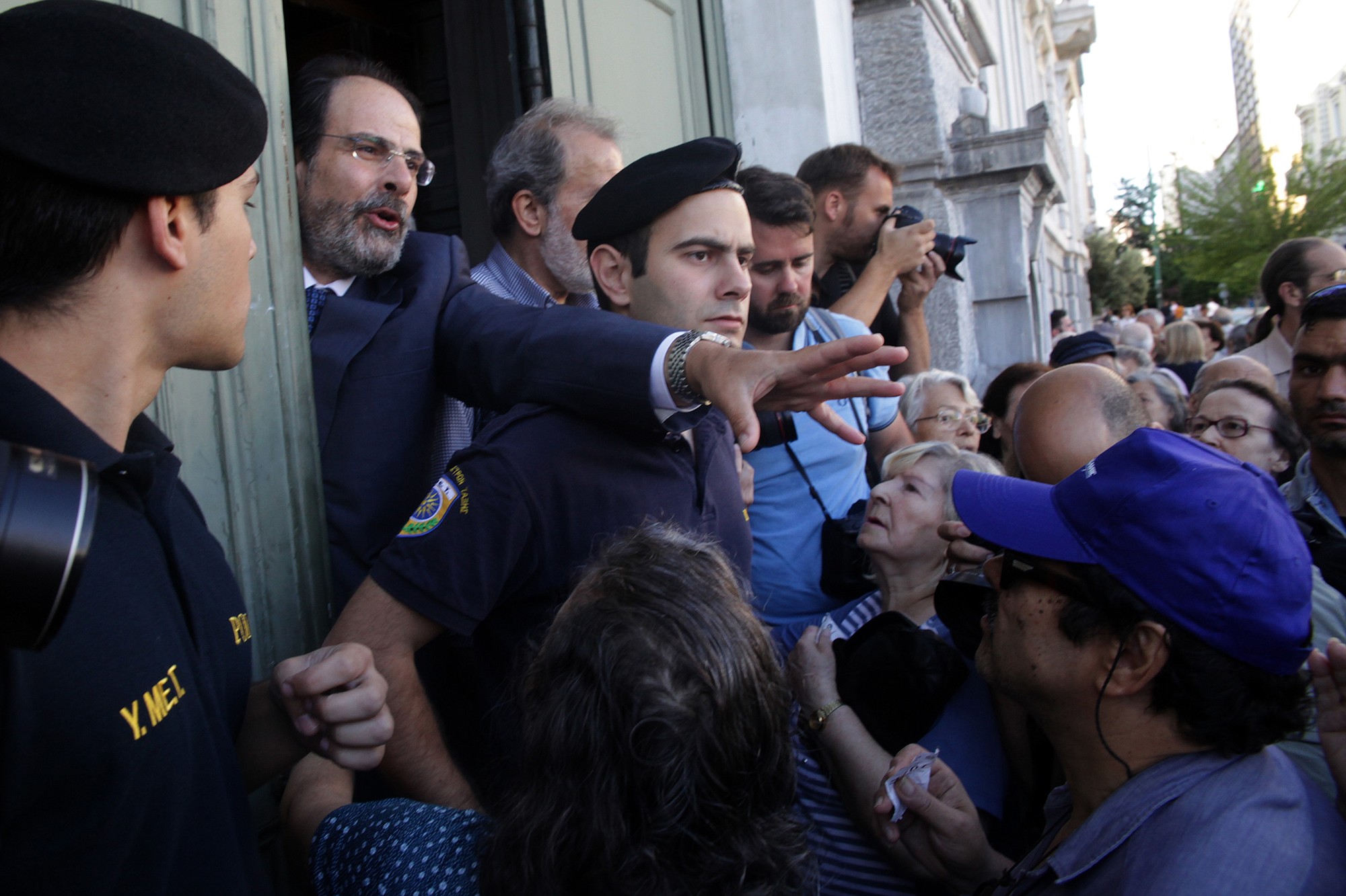 The manager of National Bank of Greece branch asks from the pensioners to stay calm at they wait to enter the building in Athens, Wednesday, July 1, 2015. Pensioners are the forgotten victims of the Greek crisis. Their monthly payments have been cut in recent years, and since many lack bank cards they were totally cut off from their funds until Wednesday?s special bank sessions allowed them partial access.