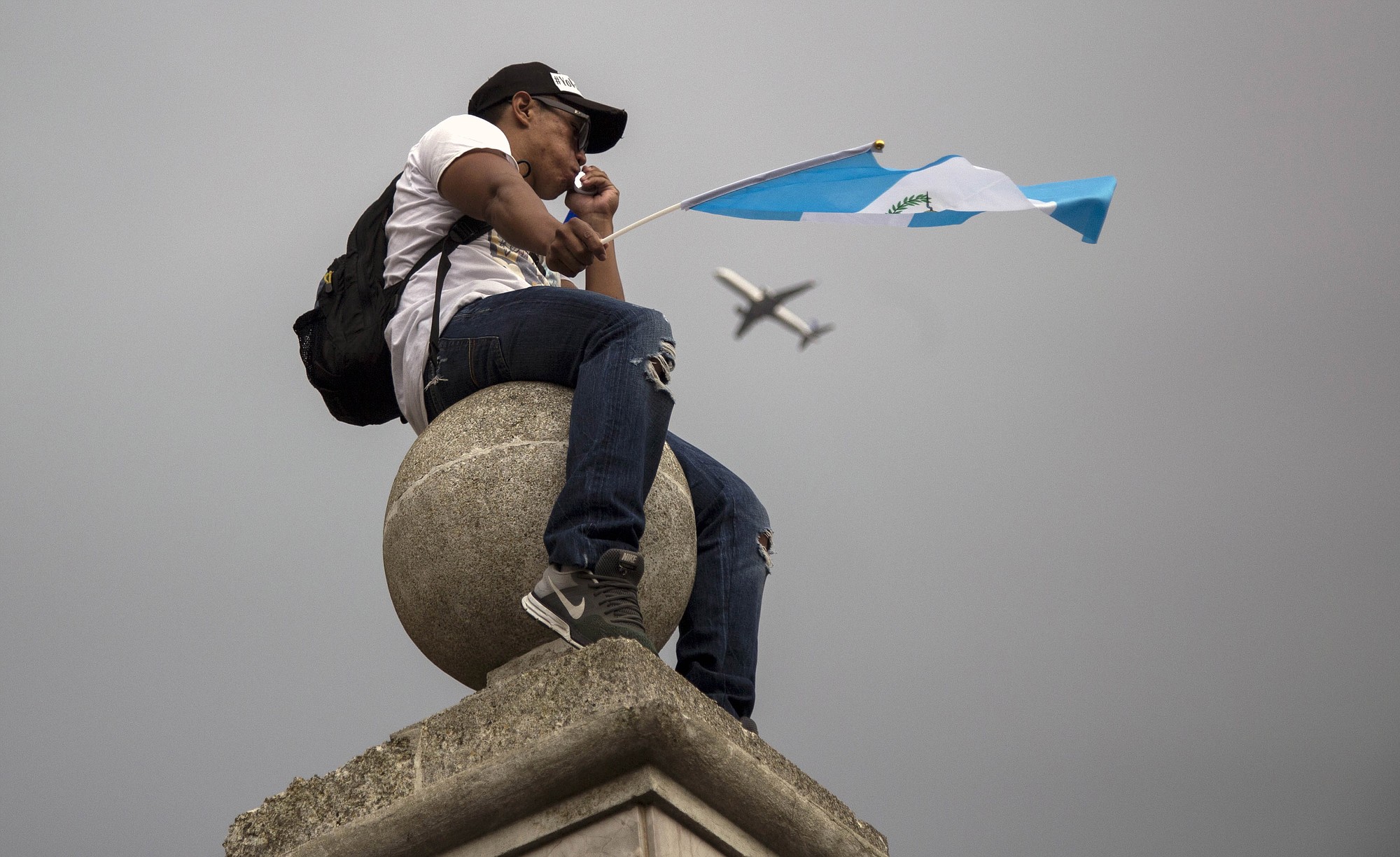 A protester waving a Guatemalan flag sits on a column at the Metropolitan Cathedral during a national strike demanding the resignation of Guatemalan President Otto Perez Molina in Guatemala City, Thursday, Aug. 27, 2015.