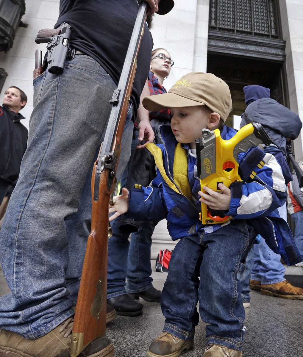 Trystan Olson, 4, of Spokane holds a toy gun as he reaches toward the trigger of the rifle of his father, Erik Olson, during a rally by gun-rights advocates at the state Capitol on Saturday in Olympia.