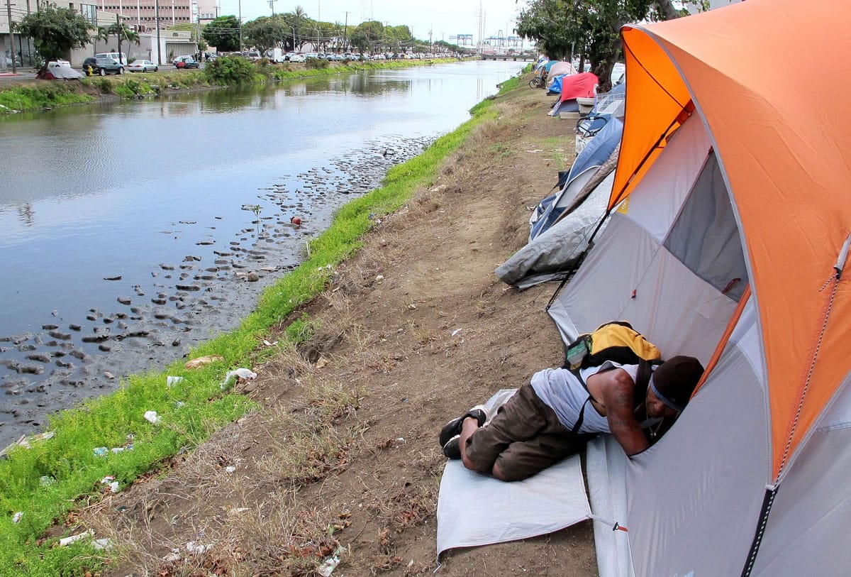 A homeless man sleeps outside a tent along a canal in Honolulu. The Honolulu City Council voted Aug.
