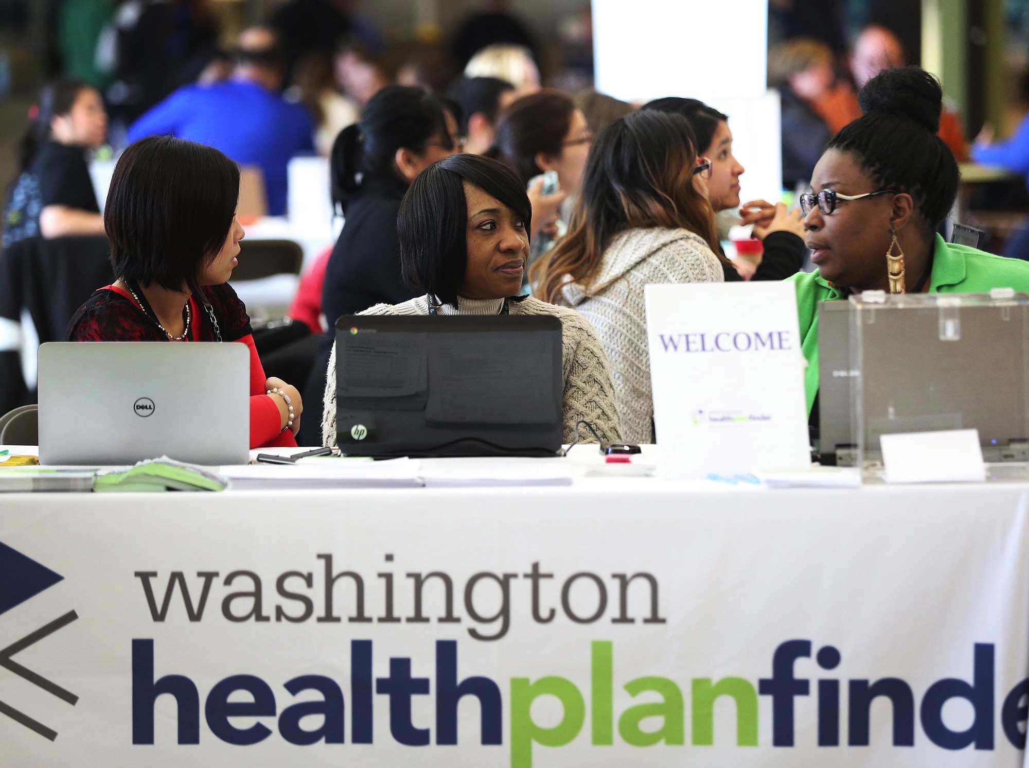 Christy An, from left, Pamela Lyons and Deborah Stanley sit at the welcome table as they wait to answer questions during a Washington Healthplanfinder sign-up event at Westfield Southcenter in Tukwila, on Saturday.