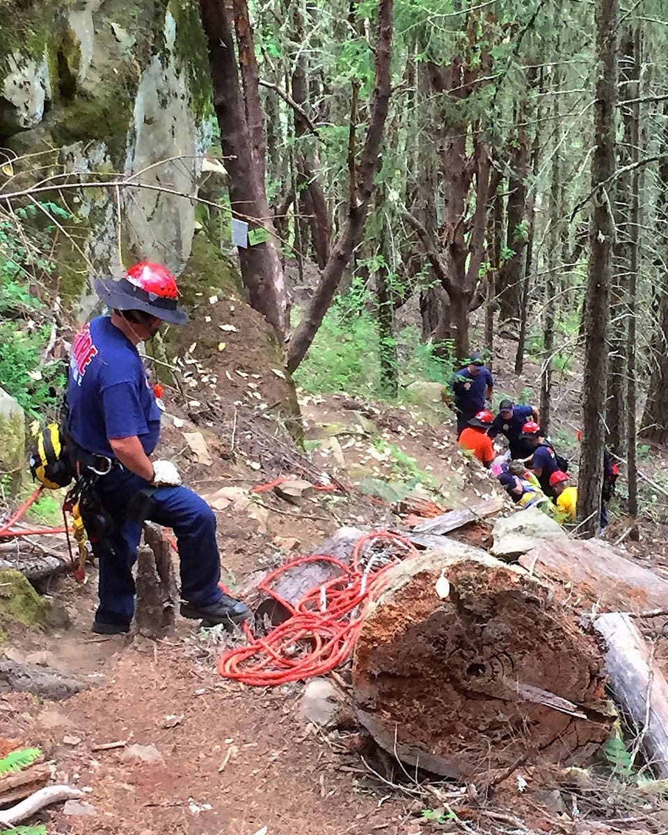 In this July 4, 2015, photo provided by Greg Suhrstedt, a firefighter observes as other rescuers treat injured Daniel Cooper after he fell from a huge rock next to the trail on the Callahan mountain range west of Roseburg, Ore.