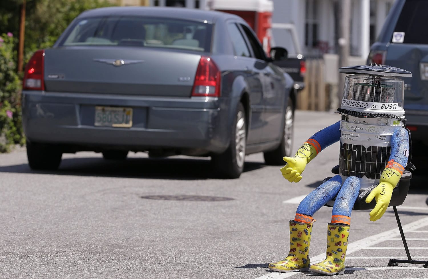 A car drives by HitchBOT, a hitchhiking robot in Marblehead, Mass.
