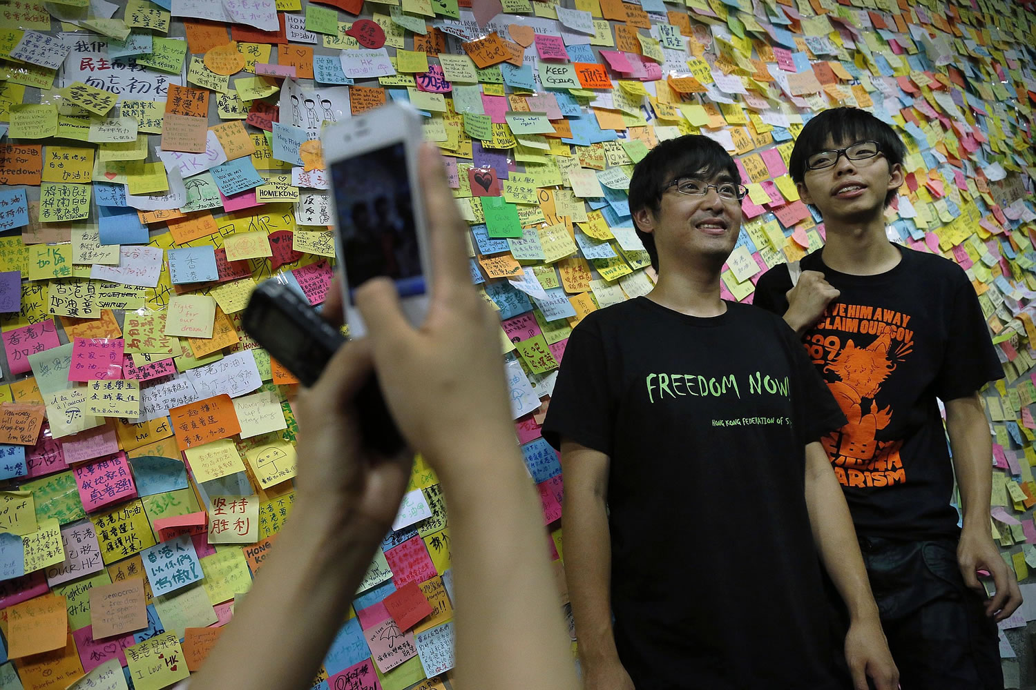Hong Kong democracy protesters stand in front of a billboard covered in notes on Post-Its.