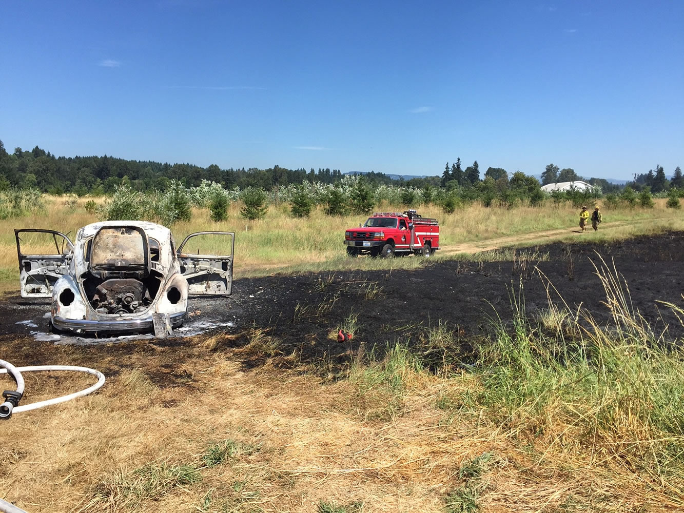 Remains of a burned-out Volkswagen Beetle sit in a field after a car fire spread to dry grass off Northeast 259th Street on Thursday.