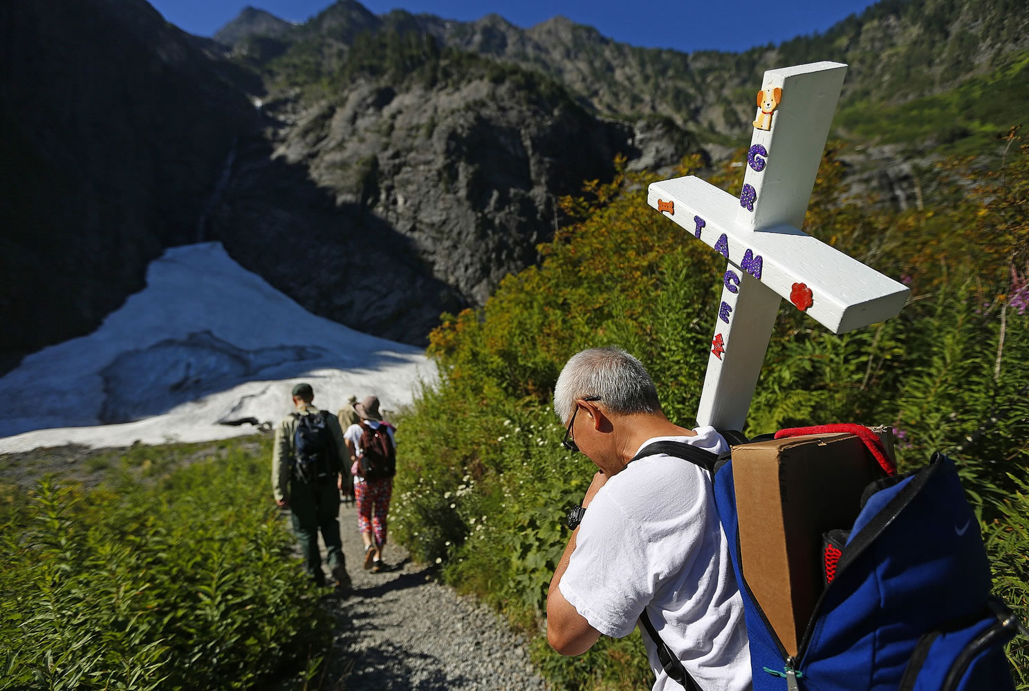 John Tam carries a cross bearing the name of his daughter, Grace, as he hikes the mile to the Big Four ice caves Thursday in Verlot, where Grace, 11, died July 31, 2010, from internal injuries after a piece of ice fell on her. Tam tried to auger the cross into the ground but the rocky spot was too stubborn; he plans to return another day to finish the job. One lavender cross already marks the spot.