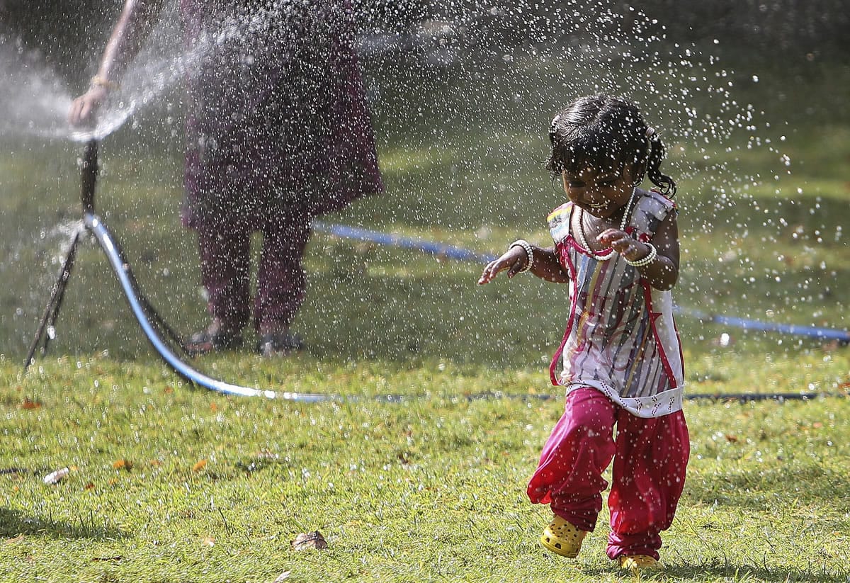 An Indian child plays in front of a water sprinkler to cool off on a hot summer day at Nehru Zoological Park in Hyderabad, India, on Friday,.