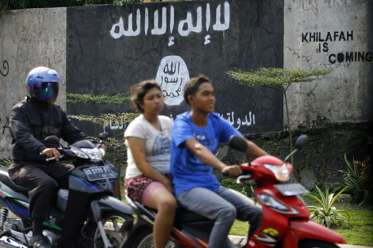 Motorists ride past a graffiti of the Islamic State group's flag in Solo, Central Java, Indonesia.