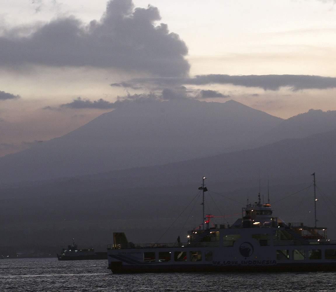 Aferry boat crosses the Bali Strait to carry Indonesians to Ketapang port, East Java, from Gilimanuk port, West Bali, Indonesia as Mount Raung spews volcanic smoke.