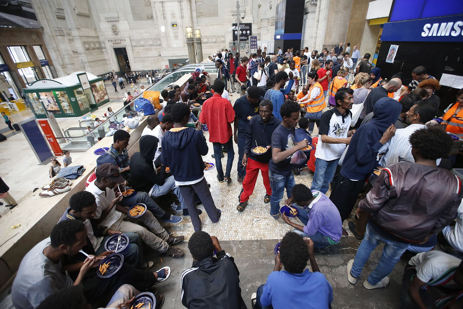 Migrants eat in the Central railway station Thursday in Milan, Italy.