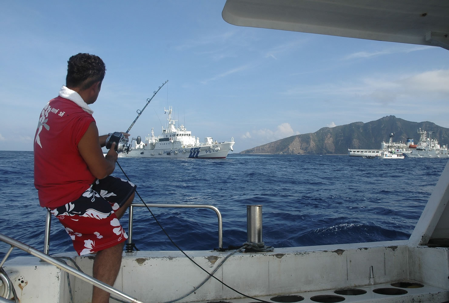 Associated Press files
A Japanese activist fishes from a boat in August 2013 near a group of disputed islands called the Senkaku by Japan and Diaoyu by China. Japanese Coast Guard vessels are seen in the background.