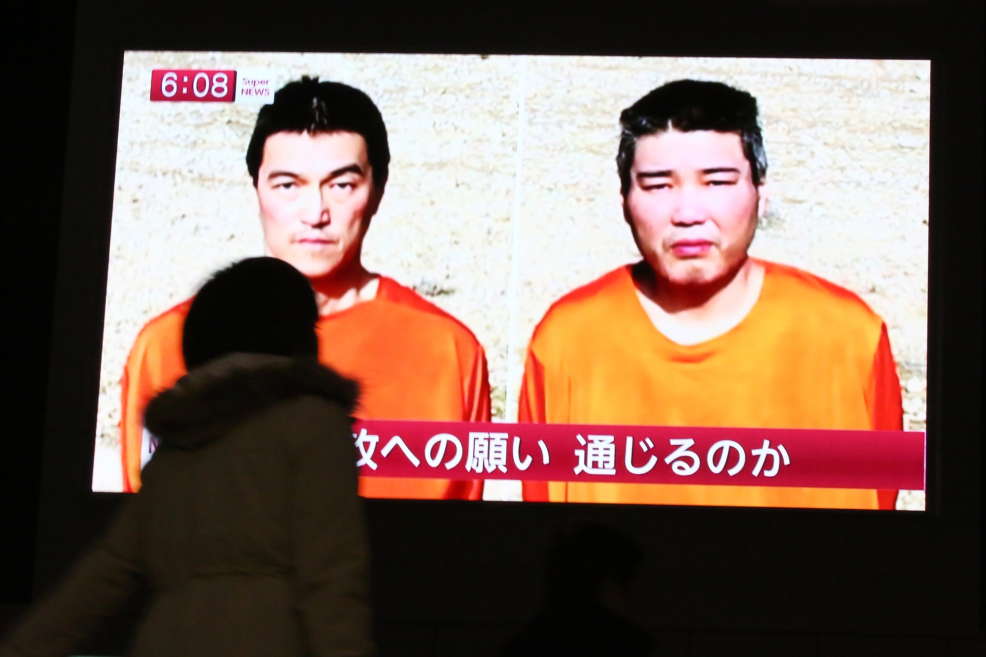 A passer-by in Tokyo watches a TV news program Friday reporting on two Japanese hostages, Kenji Goto, left, and Haruna Yukawa, held by the Islamic State group. Militants affiliated with the Islamic State group have posted an online warning that the &quot;countdown has begun&quot; for the group to kill the pair.