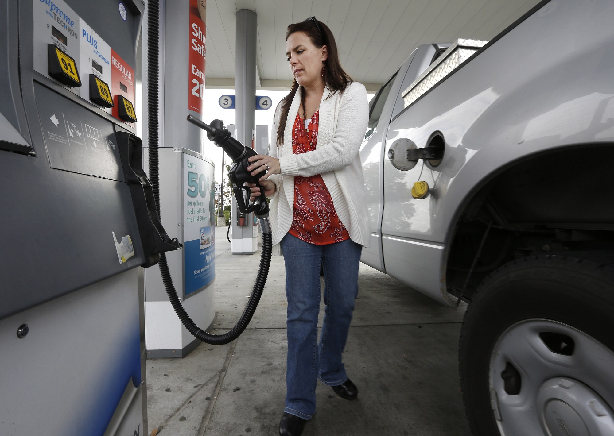 Lydia Holland replaces the gas nozzle after filling up at a gas station in Sacramento, Calif. The Energy Department on Tuesday again slashed its prediction for next year?s average price of gasoline across the U.S., this time to $2.60 a gallon. That's 23 percent below the projected average for this year and the lowest since 2009.