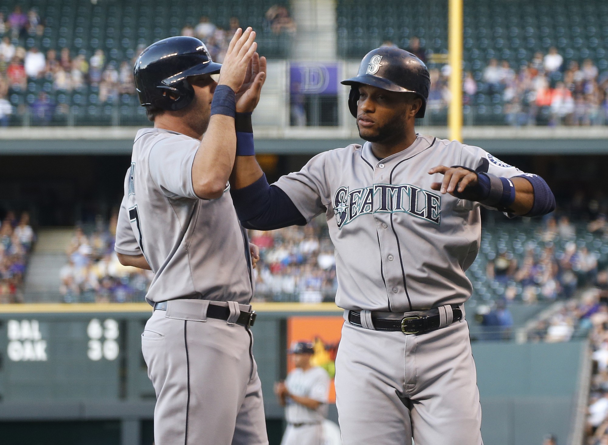 Seattle Mariners' Seth Smith, left, is congratulated by Robinson Cano after they scored on a double by Jesus Montero against the Colorado Rockies in the first inning Monday, Aug. 3, 2015, in Denver.
