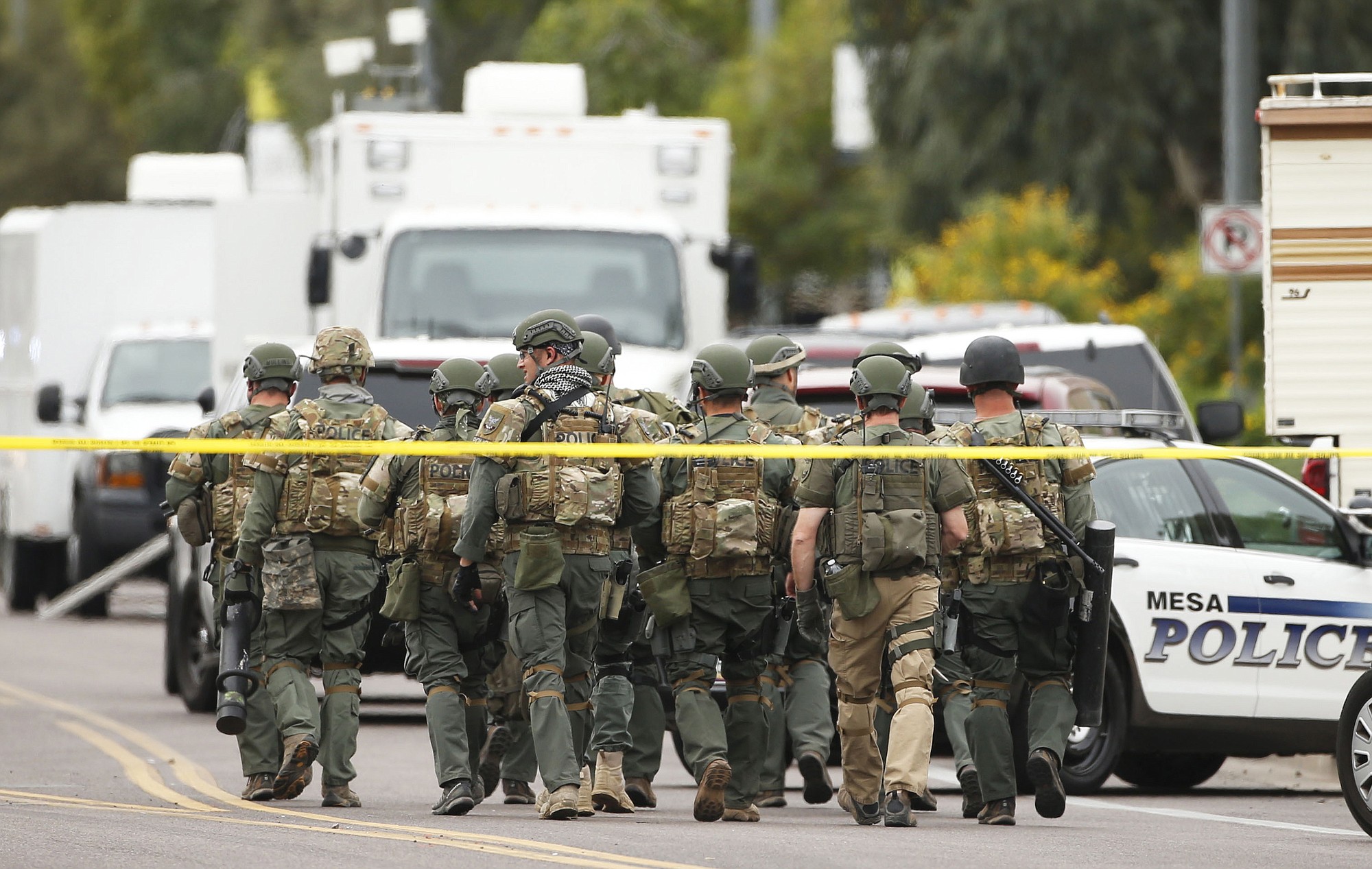 A SWAT team walks down the street near Adams Elementary School searching for a gunman on Wednesday, March 18, 2015 in Mesa, Ariz. A gunman wounded at least four people across multiple locations in the Phoenix suburb. The first shooting happened at a motel, and people were also wounded at a restaurant and nearby apartment complexes.
