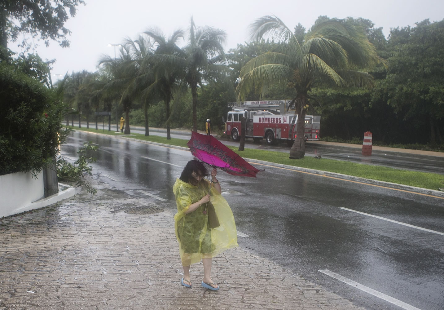 A woman has her umbrella twisted by the strong winds of tropical storm Carlos, as she walks down the main hotel strip in Cancun, Mexico, Sunday, June  14, 2015.