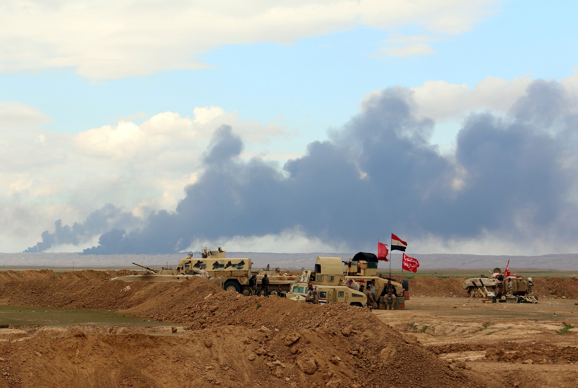 In this Wednesday, March 4, 2015 photo, smoke rises as the Iraqi army, supported by volunteers, battles Islamic State extremists outside Tikrit, 80 miles (130 kilometers) north of Baghdad, Iraq. Iranian-backed Shiite militias and Sunni tribes have joined Iraq's military in a major operation to retake Tikrit from the Islamic State group, while the U.S. led coalition has remained on the sidelines.
